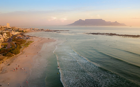 group of people near ocean water and mountains under blue and white cloudy sky during daytime thumbnail