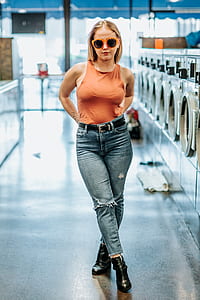 woman wearing orange sleeveless top and blue denim jeans standing near front-load laundry appliances thumbnail