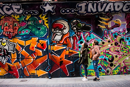 two women staring at graffiti on wall thumbnail