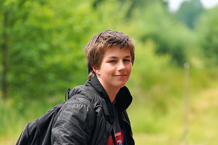 boy wearing black jacket and backpack standing near plant thumbnail