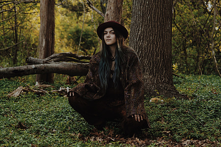 woman wearing brown coat and red hat sitting near trees thumbnail