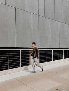 man wearing brown long-sleeved shirt walking near wall at daytime thumbnail