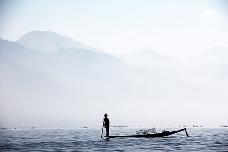 silhouette of man standing on boat near mountain thumbnail
