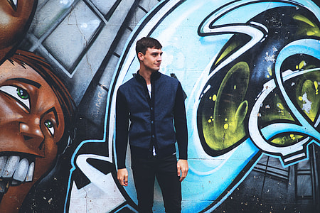 A man stands by a wall covered in street art thumbnail