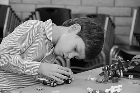 grayscale photo of a boy wearing pinstriped button-up long-sleeved dress shirt vehicle plastic toy on table thumbnail