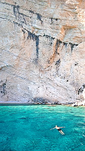 man floating on sea near cliff thumbnail