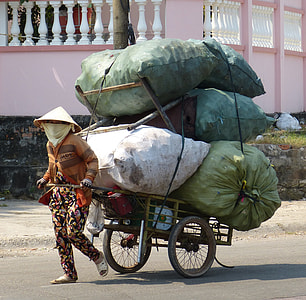 person carrying bicycle trailer with pile of sack at daytime thumbnail