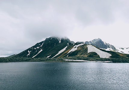 photography of mountains cover by trees near ocean under white sky at daytime thumbnail