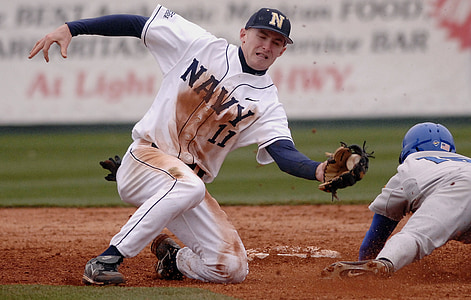 Navy 11 baseball player catching ball while kneeling near base duting daytime thumbnail