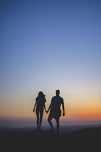 silhouette of man and woman holding hands standing surface at golden hour thumbnail
