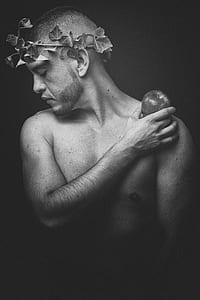 greyscale photo of topless man wearing leaf headdress while holding apple thumbnail
