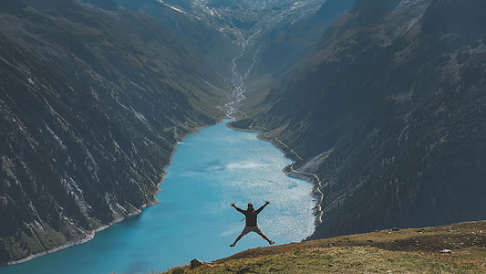 man jumping on top of mountain in a distance of a river thumbnail