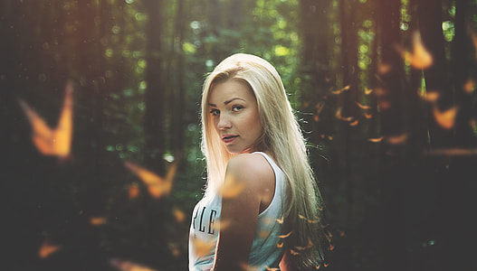 tilt-shift lens photography of woman wearing white tank top surrounded by butterflies outdoors thumbnail