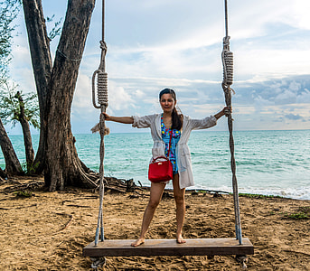 woman wearing white long sleeve vest on black and gray swing near ocean thumbnail