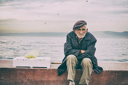 man wearing black jacket and brown pants sitting on seashore thumbnail
