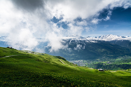 mountain slope covered with grass with a view of a mountain covered with snow under blue skies landscape photography thumbnail