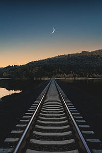 gray train track leading to mountain under blue sky thumbnail