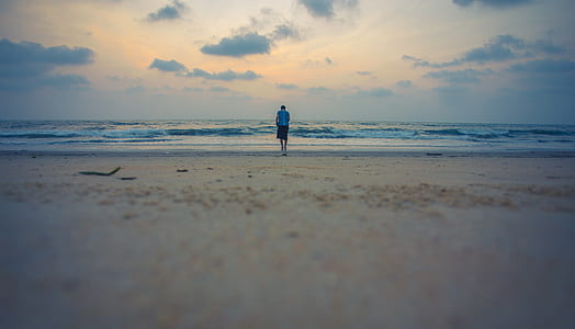 man walking through beach under cloudy sky thumbnail