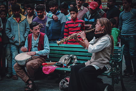 woman playing wind instrument sitting next to man with drum surrounded by people thumbnail