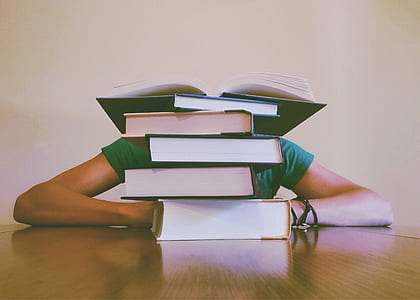 person sitting in front of piled of books on top of table thumbnail