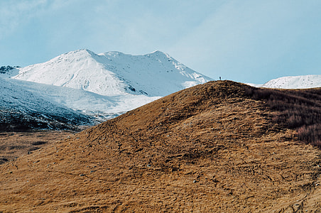 person standing on hill looking to snow covered mountain thumbnail
