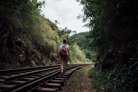 woman wearing white t-shirt walking on train trail during daytime thumbnail