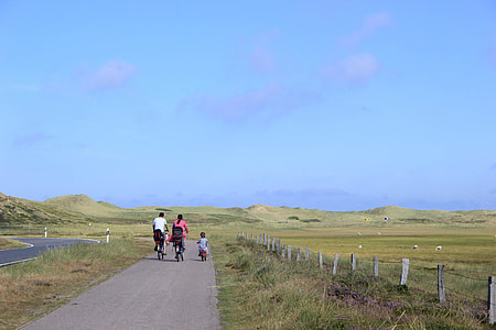 children, woman, and woman bicycling on road beside field thumbnail