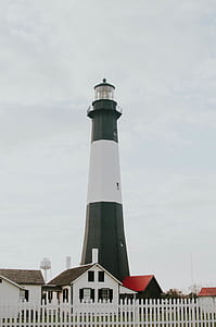 white and black lighthouse near beside white and red house under white cloud thumbnail