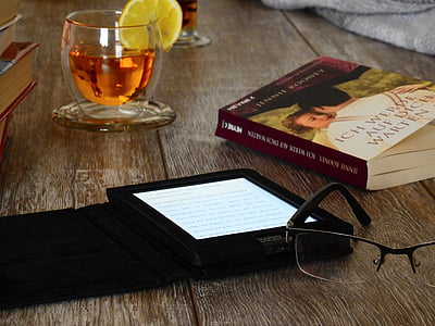eyeglass beside e book reader and book on brown wooden surface thumbnail