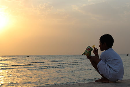 boy squatting in front calm body of water at sunset thumbnail