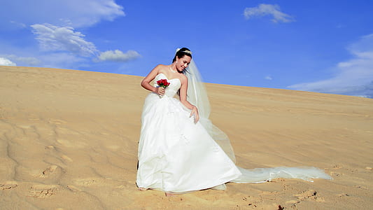 woman wearing white wedding dress standing on sand desert thumbnail