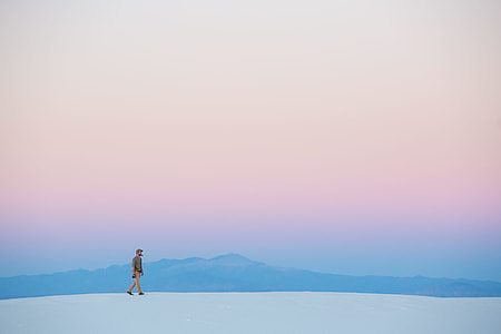 man walking on white sand far from mountains thumbnail