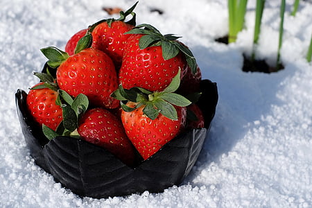 strawberries in round black foliage ceramic bowl half buried on snow at daytime thumbnail