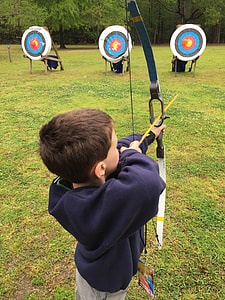 boy using composite bow aiming on target on green grass during daytime thumbnail