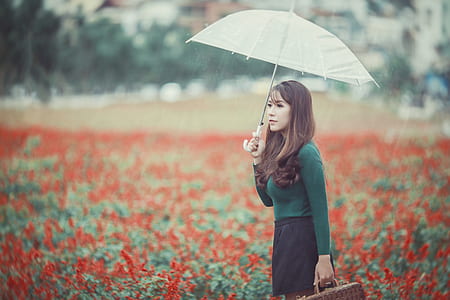 woman wearing green long-sleeved shirt holding grey umbrella in red petal flower garden thumbnail