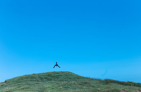 person jumping on hill under blue sky thumbnail
