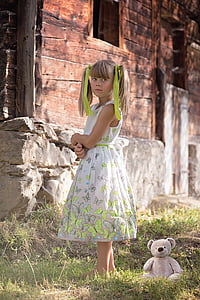 photo of girl wearing white dress standing on grass beside brown bear plush toy thumbnail