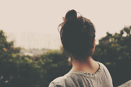 shallow focus photography of woman in grey shirt with bun hairstyle facing green trees thumbnail