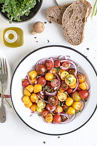 slice tomatoes and onions salad on white plate beside bread and silver fork thumbnail