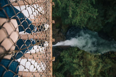 Receding perspective view of legs on a caged-design metal bridge over water thumbnail