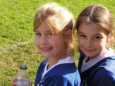 two girl wearing white and blue v-neck shirts standing on green grass fields thumbnail