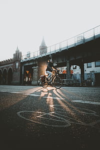 woman wearing black jacket and gray pants cycling near gray concrete bridge thumbnail