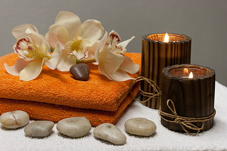 white orchids and two brown candles on top of orange towel closeup photography thumbnail