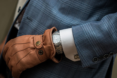 person wearing round gold-colored analog watch, brown leather glove and blue suit jacket thumbnail