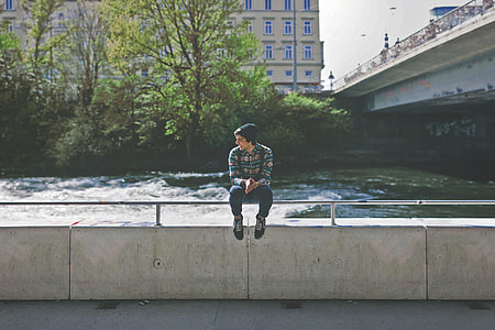 man in green and brown dress shirt sitting on grey metal hand rail near river thumbnail