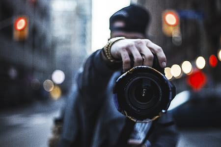 tilt shift photo of man holding camera surrounded with buildings thumbnail