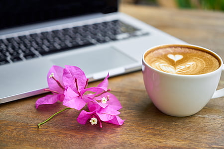 pink bougainvillea flower beside cup of coffee and silver laptop computer on brown wooden table thumbnail