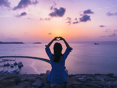 Woman Sitting on Rock Doing Heart Hand Gesture thumbnail