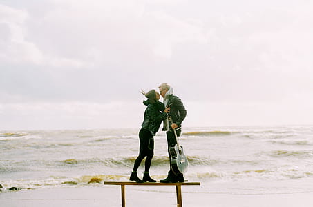 Woman Kissing Man Holding Guitar Beside Beach thumbnail