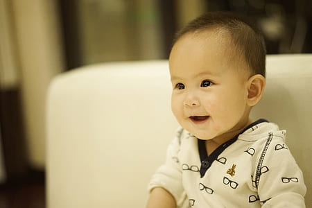 smiling baby sitting on white chair thumbnail